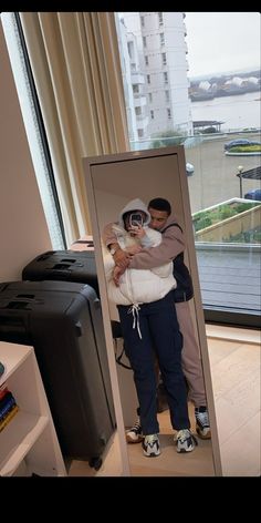 two people standing in front of a mirror with their arms around each other and one person holding a baby