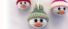 three crocheted snowman ornaments hanging on a white wall, one wearing a green and red hat