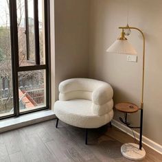 a white chair sitting in front of a window next to a lamp