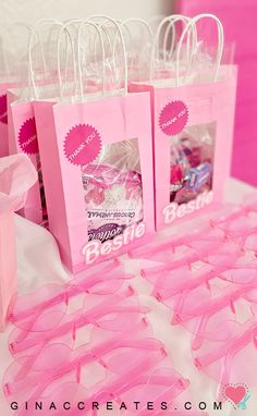 pink paper bags with bows and ribbons are on a white tablecloth, next to some candy