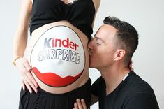 a man kissing a pregnant woman's belly with the words kinder surprise written on it