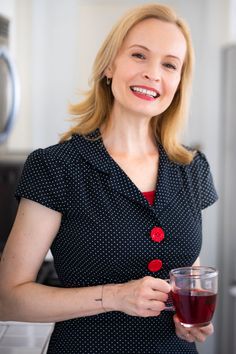 a woman holding a glass of red wine in her hand and smiling at the camera