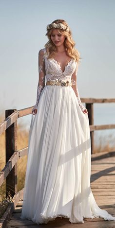 a woman in a long white dress standing on a wooden bridge with her hands on her hips