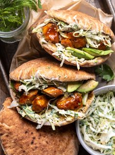 two pita sandwiches with coleslaw slaw and avocado on the side