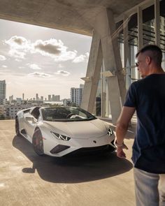 a man standing next to a white car in front of a tall building with windows