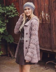 a woman wearing a knitted coat and hat standing in front of a rusty building