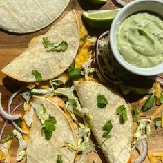 several tortillas with guacamole and onions on a wooden cutting board