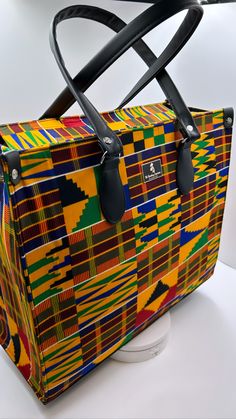 This posh farmer's market bag is for those farmers market visits where you want to be posh, stylish and still be eco-friendly. It's made out of wax print kente cloth, with durable handle, reinforced bottom and Interior pocket with generous capacity, 14"H x 16.2" L x 7" W. Our luxurious handmade handbags are made from vibrantly stunning wax print West African fabric, they're expertly and beautifully crafted handbags with vegan leather base and double stitched to ensure long durability and longevi Rectangular Travel Bag With Detachable Handle For Shopping, Top Handle Shoulder Bag With Reinforced Handles For Shopping, Rectangular Weekender Bag With Leather Handles, Rectangular Travel Bag With Top Carry Handle, Yellow Rectangular Box Bag For Travel, Yellow Square Box Bag For Travel, Adjustable Handle Tote Box Bag For Shopping, Yellow Square Bag For Market, Rectangular Box Bag With Leather Handles For Shopping