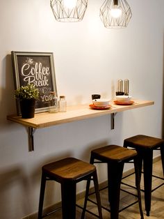 three stools are sitting on the counter in front of a coffee bar with lights above it