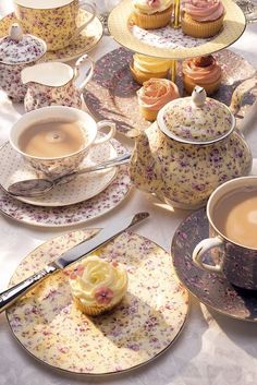 a table topped with plates covered in cupcakes next to cups and saucers