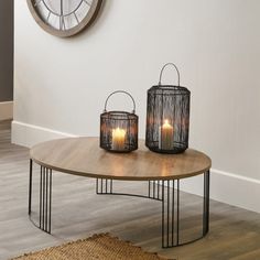 two lit candles sit on a table in front of a clock