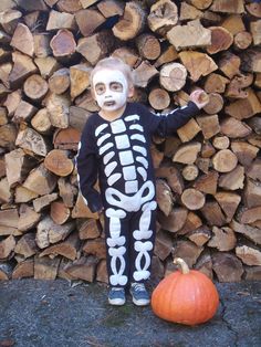 a skeleton doll standing next to a pile of firewood in front of a pumpkin