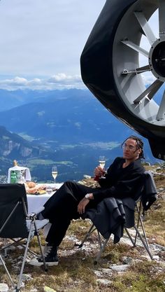 a man sitting on top of a mountain next to a table with food and drinks