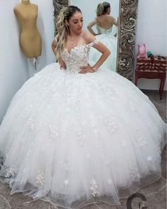 a woman standing in front of a mirror wearing a wedding dress with flowers on it