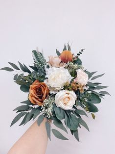 a woman's hand holding a bouquet of white and orange flowers with greenery