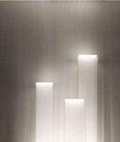 three rectangular lights are lit up in a room with white walls and flooring on either side