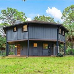 a gray house sitting in the middle of a lush green field with trees around it