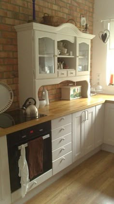 a kitchen with white cabinets and wood floors in front of a brick wall is shown