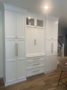 a kitchen with white cupboards and chairs in the middle of it, along with hardwood floors