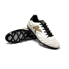 a pair of white and black soccer shoes with gold accents on the soles, against a white background