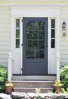 the front door of a white house with black glass and two pots on the steps