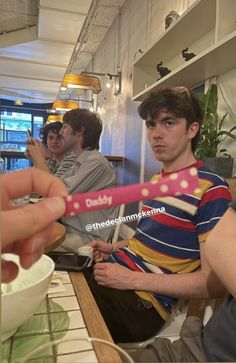 a man holding a toothbrush in his hand while sitting at a table with other people