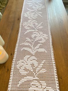 the table runner is made with white crochet and sits on top of a wooden table