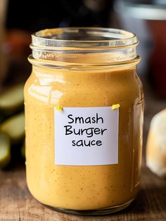 a jar filled with mustard sitting on top of a wooden table next to sliced cucumbers