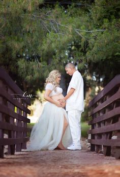 a pregnant couple standing on a bridge in front of some trees and looking into each other's eyes