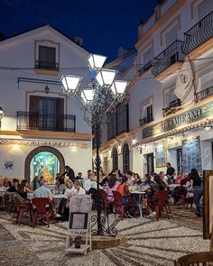 many people are sitting at tables in an outdoor dining area with chandelier above them