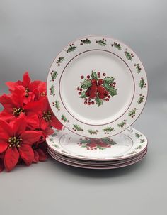 a stack of plates with holly and poinsettis on them next to red flowers