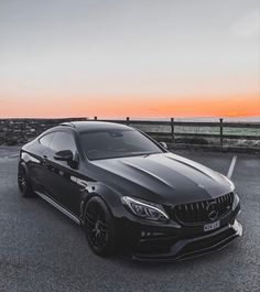 a black car parked in a parking lot next to the ocean at sunset or dawn