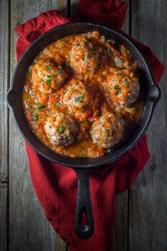 meatballs and sauce in a cast iron skillet on a red cloth next to a wooden table