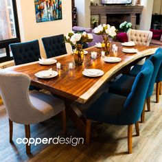 a dining room table with blue chairs and white plates on it, in front of a fireplace