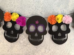 three paper skulls with colorful flowers on them hanging from a string in front of a wall