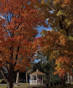 a gazebo in the middle of a park surrounded by trees with orange and yellow leaves