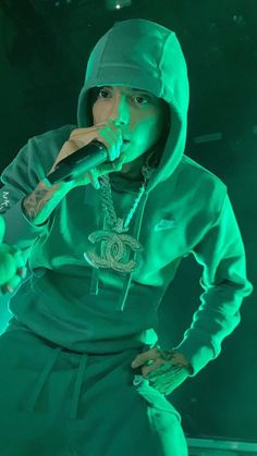 a man in a green hoodie is holding a microphone and wearing a chain around his neck