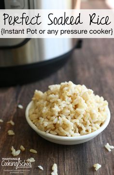 rice in a white bowl next to an instant pot on a wooden table with grain scattered around it