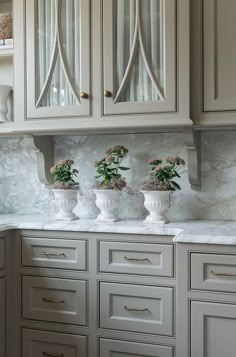 three white vases with flowers in them on a marble counter top next to cabinets