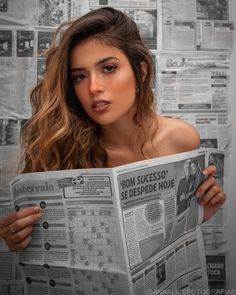 a beautiful young woman reading a newspaper while holding it up to her face and looking at the camera