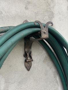 a green hose connected to a metal hook on the side of a white stucco wall