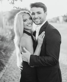 a man and woman hugging each other in front of a tree on a brick road