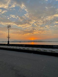 the sun is setting behind a street light on the side of the road with water in the background