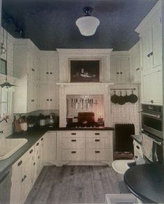 an old photo of a kitchen with white cabinets and black counter tops, along with wood flooring