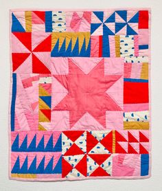 a pink and blue patchwork quilt hanging on a wall