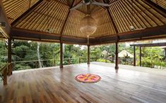 a large open room with wooden floors and thatched roof, surrounded by greenery