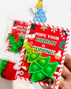 a hand holding up a christmas card with holiday decorations on it and an ornament in the shape of a tree