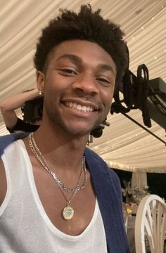 a man wearing a white tank top standing in front of a camera and smiling at the camera