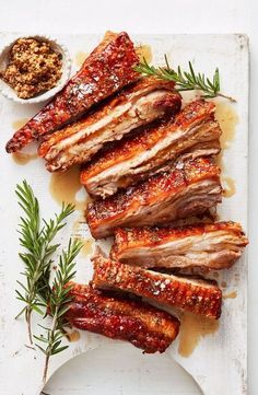 ribs with sauce and herbs on a white plate next to a small bowl of seasoning