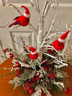 a vase filled with red birds sitting on top of a table next to a white tree